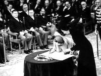 Koningin Juliana ondertekent in de Ridderzaal het Statuut. Naast haar staat mevrouw Tellegen, directeur van het Kabinet der Koningin.